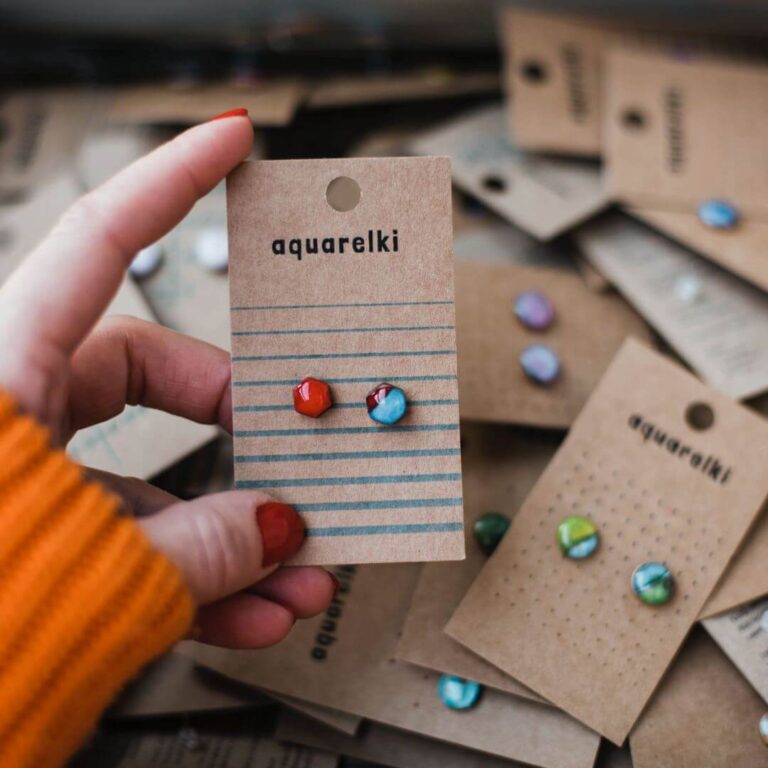 Kolczyki Aquarelki z akwareli trzymane w ręce w tle inne kolczyki z akwareli